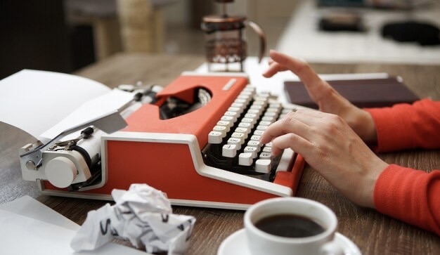 Side view of red typewriter, cup of coffee, crumpled paper